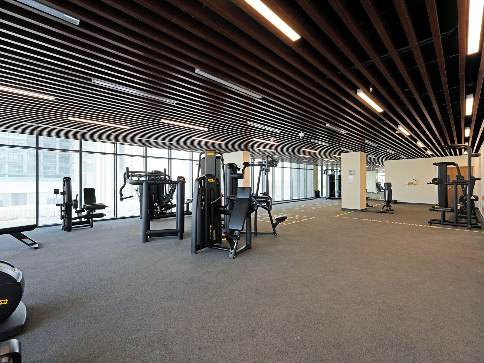 Uma academia espaçosa com diversos equipamentos de exercício, janelas amplas e um design moderno no teto.