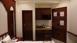 Habitación de hotel con cama, mesita de noche con lámpara, kitchenette pequeña con microondas y armario de madera.