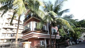 Un edificio de varios pisos con balcones, rodeado de palmeras y una entrada con portones.