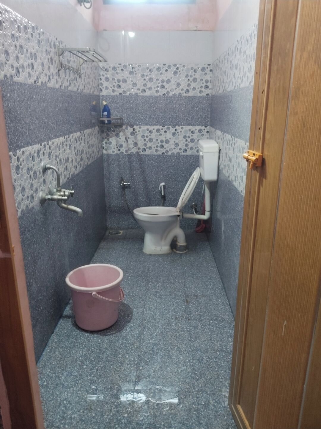 Een kleine badkamer met toilet, douche en een roze emmer.