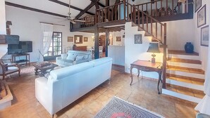 A spacious living room with a high ceiling, a staircase leading to an upper level, and a television on a stand. - La Maisonnette by Interhome (Le Val)