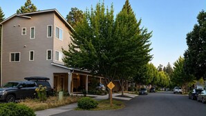 Une rue résidentielle bordée de maisons, avec des voitures garées et un ciel dégagé.