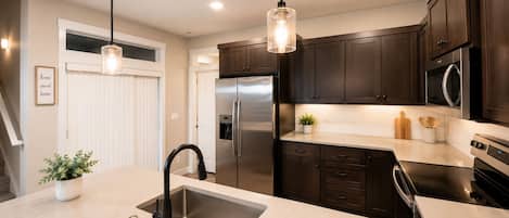 A modern kitchen with stainless steel appliances, dark wooden cabinets, and pendant lighting.