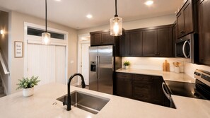 A modern kitchen with stainless steel appliances, dark wooden cabinets, and pendant lighting. - Cozy and Peaceful Queen's Bedroom 1 (Salem)