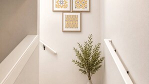 Un escalier recouvert d’une moquette beige, avec des rampes blanches et un pot de fleurs.