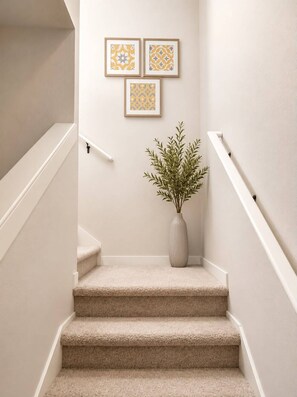 Eine Treppe mit beigem Teppich, weißen Geländern und einem Blumentopf.