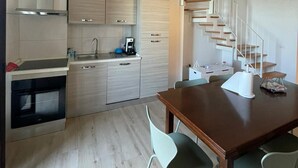 Une cuisine moderne avec des armoires en bois, un four encastré et une hotte de cuisine en acier inoxydable. On y trouve une table à manger avec quatre chaises et un escalier en colimaçon menant à un autre niveau.