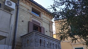 Un bâtiment doté d’un balcon orné de sculptures complexes, d’une fenêtre avec des volets en bois et d’un appareil de climatisation fixé au mur.