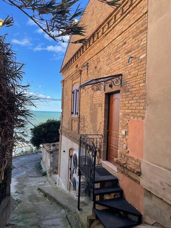A narrow stone pathway leading to a brick building with a wooden door and a small window.