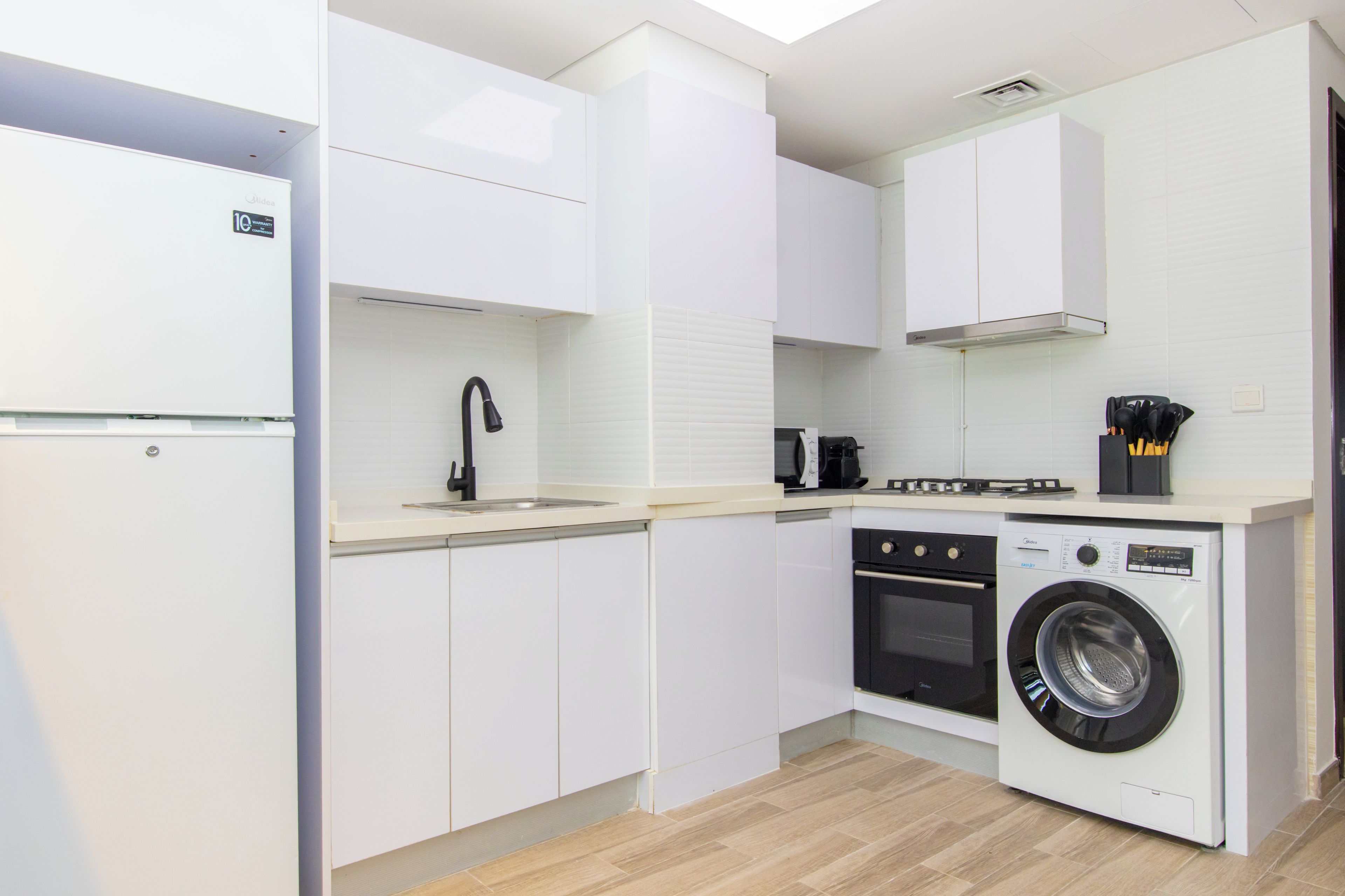 Une cuisine moderne avec des meubles blancs, un lave-linge encastré et une cuisinière à gaz.
