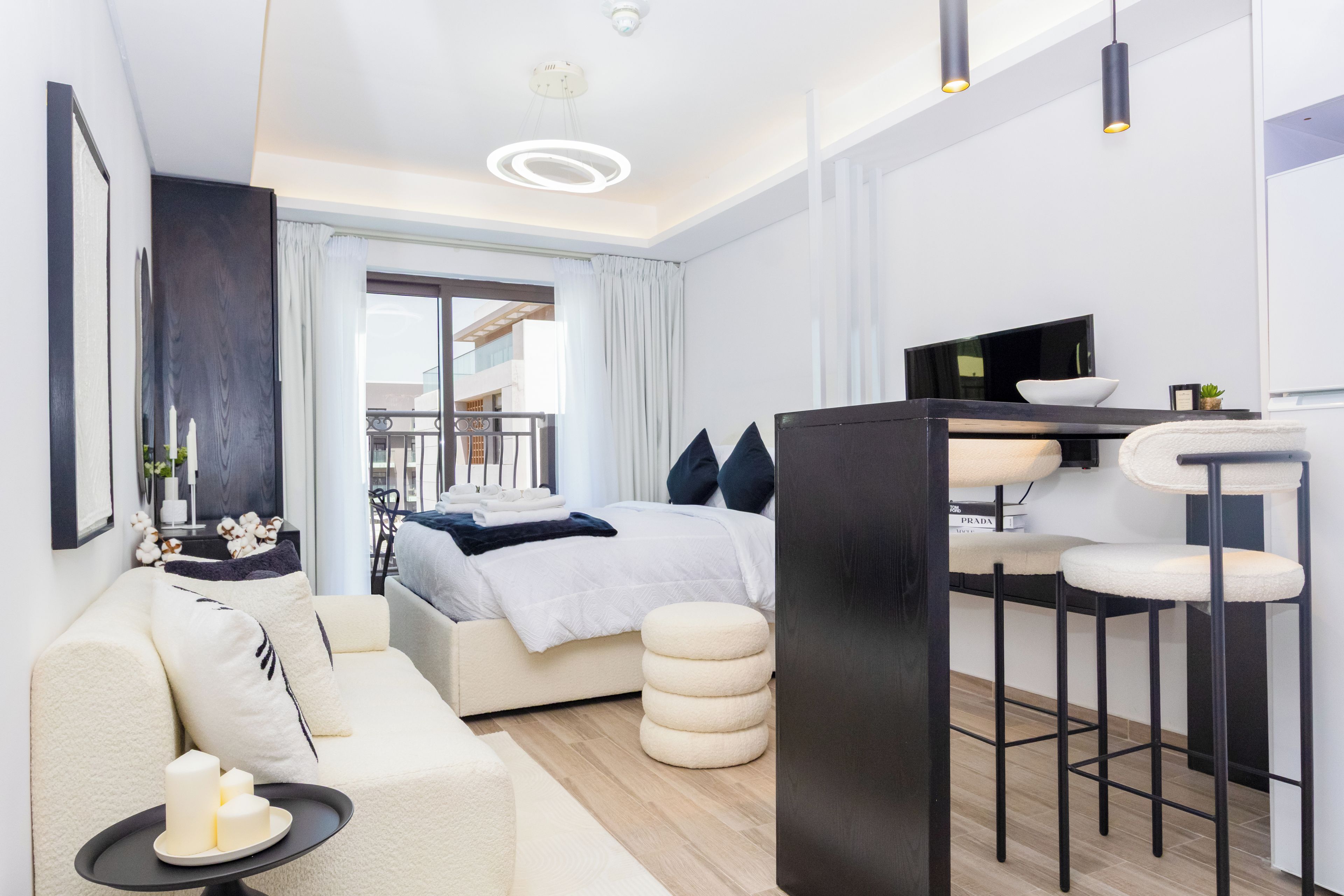 A modern hotel room with a bed, a sofa, a dining area, and a view of the outside.