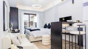 A modern hotel room with a bed, a sofa, a dining area, and a view of the outside.