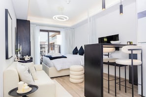 A modern hotel room with a bed, a sofa, a dining area, and a view of the outside. - Bloomfields Studio-Laya Mansion-JVC (Dubai)