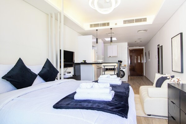 A modern hotel room with a large bed, a sitting area, a kitchenette, and a bathroom. - Bloomfields Studio-Laya Mansion-JVC (Dubai)