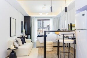 A modern hotel room with a bed, a sofa, a dining area, and a view of the cityscape. - Bloomfields Studio-Laya Mansion-JVC (Dubai)
