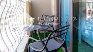 A balcony with a metal railing, a small table, two chairs, and a vase with flowers. - Bloomfields Modern Escape Stu In Jvc (Dubai)