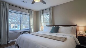 Ein Schlafzimmer mit einem Bett, Nachttischlampen, einem Deckenventilator und Fenstern mit Vorhängen.