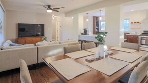 Ein modernes Wohnzimmer mit einer Sofagarnitur, einem Esstisch mit Untersetzern und einer Küche im Hintergrund.