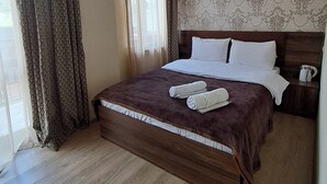 Une chambre d’hôtel avec un grand lit, une tête de lit en bois, une table de chevet, une fenêtre avec des rideaux et un mur à motifs.