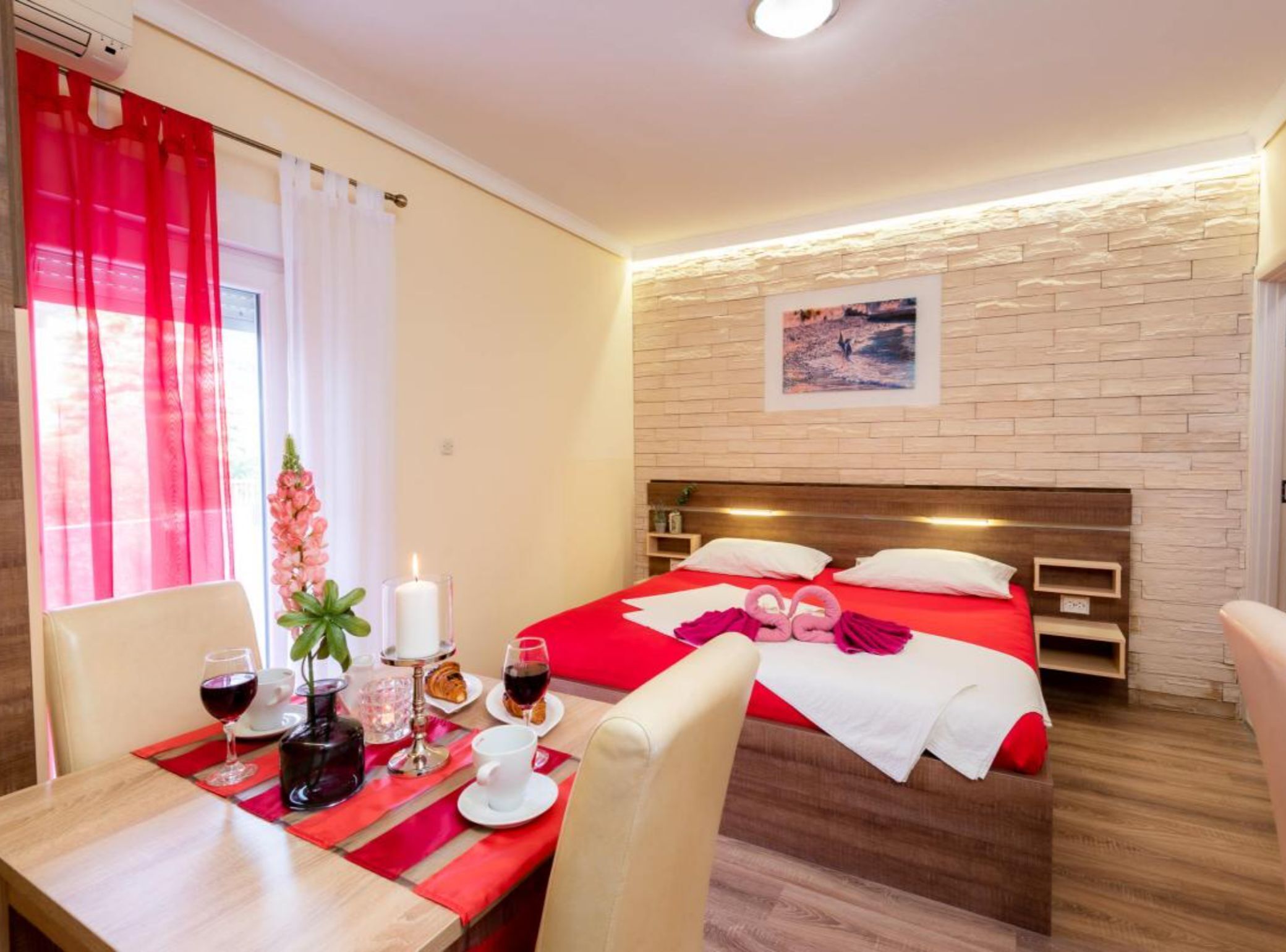 A hotel room with a bed, a table with breakfast items, a wall-mounted TV, and a window with curtains.