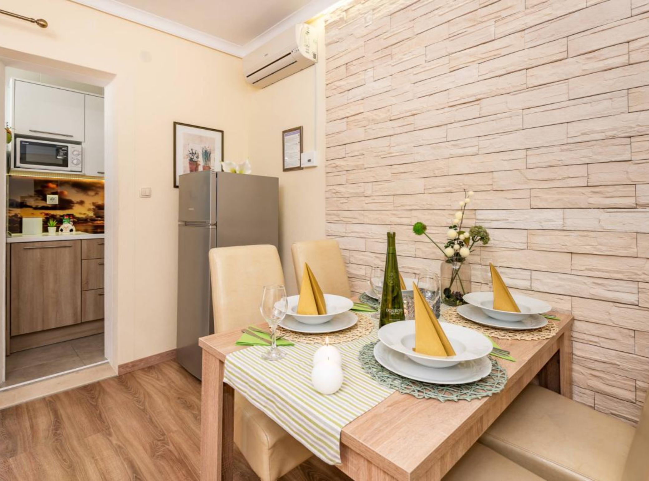 A dining area with a table set for two, a refrigerator, and a kitchen in the background.