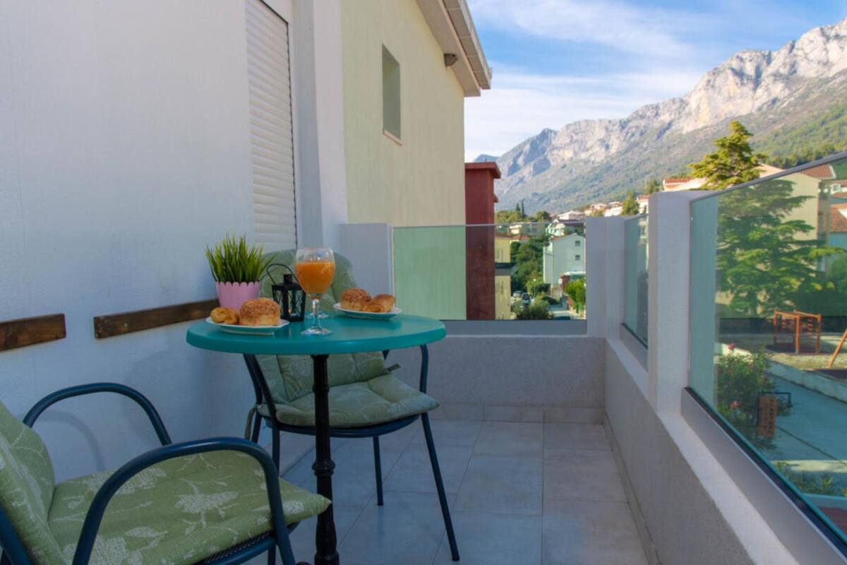 A balcony with a table set for two, chairs, a potted plant, and a glass of orange juice.