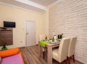 Un soggiorno moderno con zona pranzo, pavimento in legno, TV a schermo piatto montata a parete e una parete decorata con un motivo a mattoni.