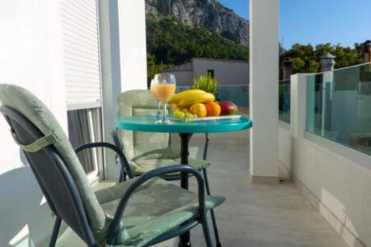 A balcony with a table set with fruits and a drink, chairs, and a mountain view.