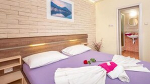 A modern hotel room with a wooden headboard, a bed with white linens, a purple bedspread, and a framed picture on the wall.
