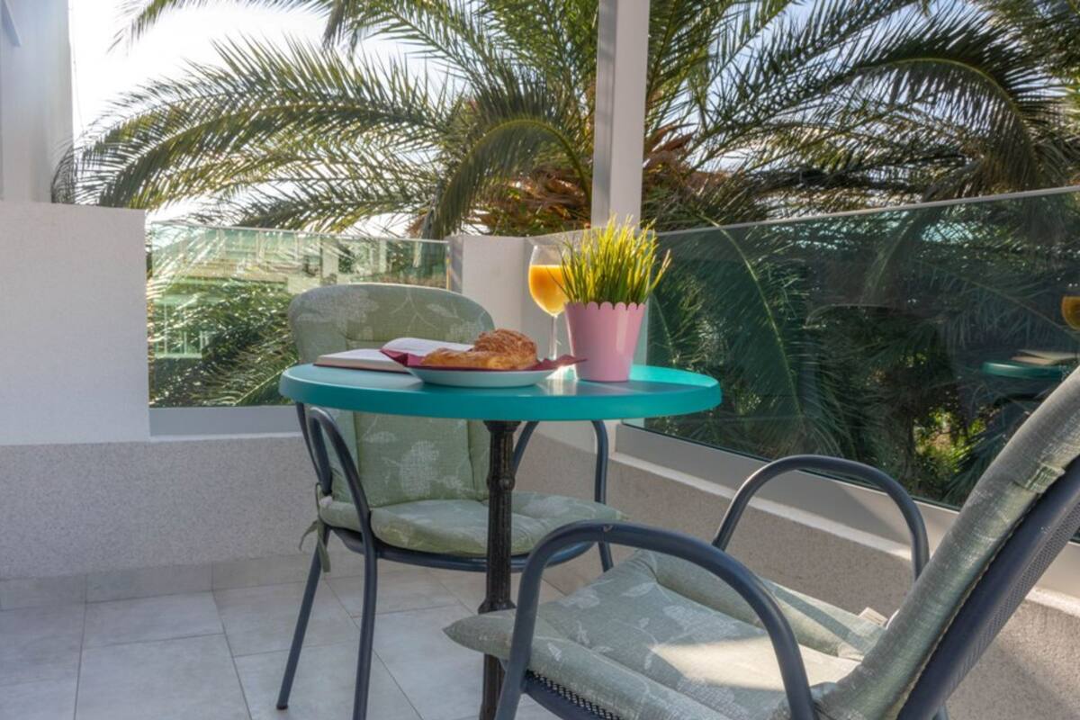 A balcony with a glass table, two chairs, a potted plant, and a plate with food.