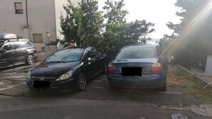 Two parked cars, a black sedan and a blue sedan, on a street with a metal grate and a building in the background. - Family-friendly Crikvenica Retreat (Crikvenica)