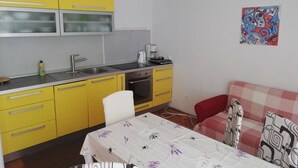 A compact kitchen with yellow cabinets, a white dining table with a floral tablecloth, and a red sofa with patterned cushions. - Family-friendly Crikvenica Retreat (Crikvenica)
