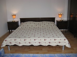 A bed with a floral-patterned bedspread, two bedside tables with lamps, and a wooden floor. - Family-friendly Crikvenica Retreat (Crikvenica)