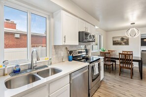 Una cocina moderna con electrodomésticos de acero inoxidable, armarios blancos y una zona de comedor con sillas de madera.