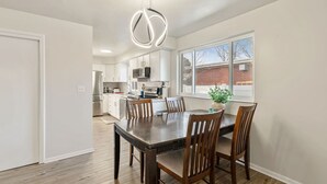 Une cuisine moderne avec des meubles blancs, des appareils en acier inoxydable et un coin repas comprenant une table et des chaises en bois.