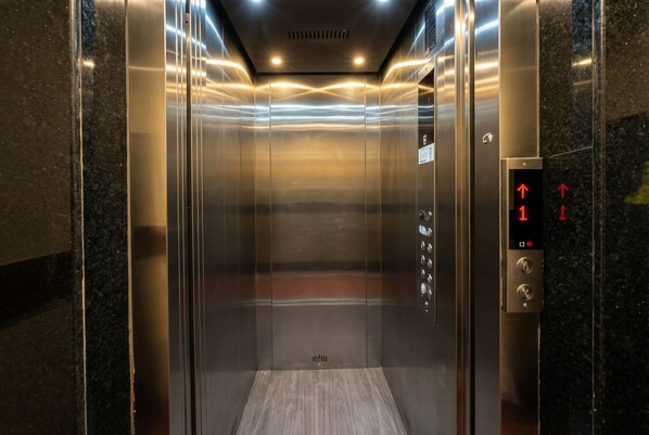 An elevator with metallic walls and a control panel with directional arrows.