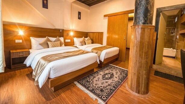 A hotel room with two beds, wooden headboards, a large pillar, and a patterned rug. - Hotel Ambrosia (Gangtok)