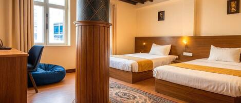 A hotel room with two beds, a desk, a chair, and a large pillar.