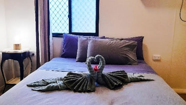 Een hotelkamer met een bed, een raam met gordijnen, een airconditioning en een klein tafeltje met een lamp.