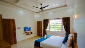 A bedroom with a bed, a television, a ceiling fan, and a window with curtains. - Hazeberg Resort Munnar (Devikolam)