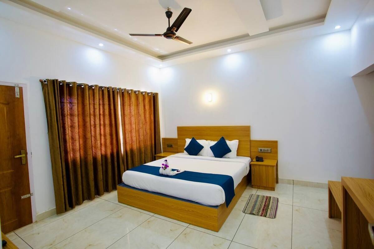 Una habitación de hotel con una cama de madera, un ventilador de techo, una mesita de noche y una pequeña mesa de madera.