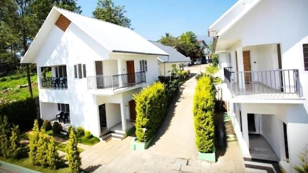 A modern residential building with a symmetrical design, featuring two-story structures with balconies, a central pathway, and neatly trimmed greenery. - Hazeberg Resort Munnar (Devikolam)