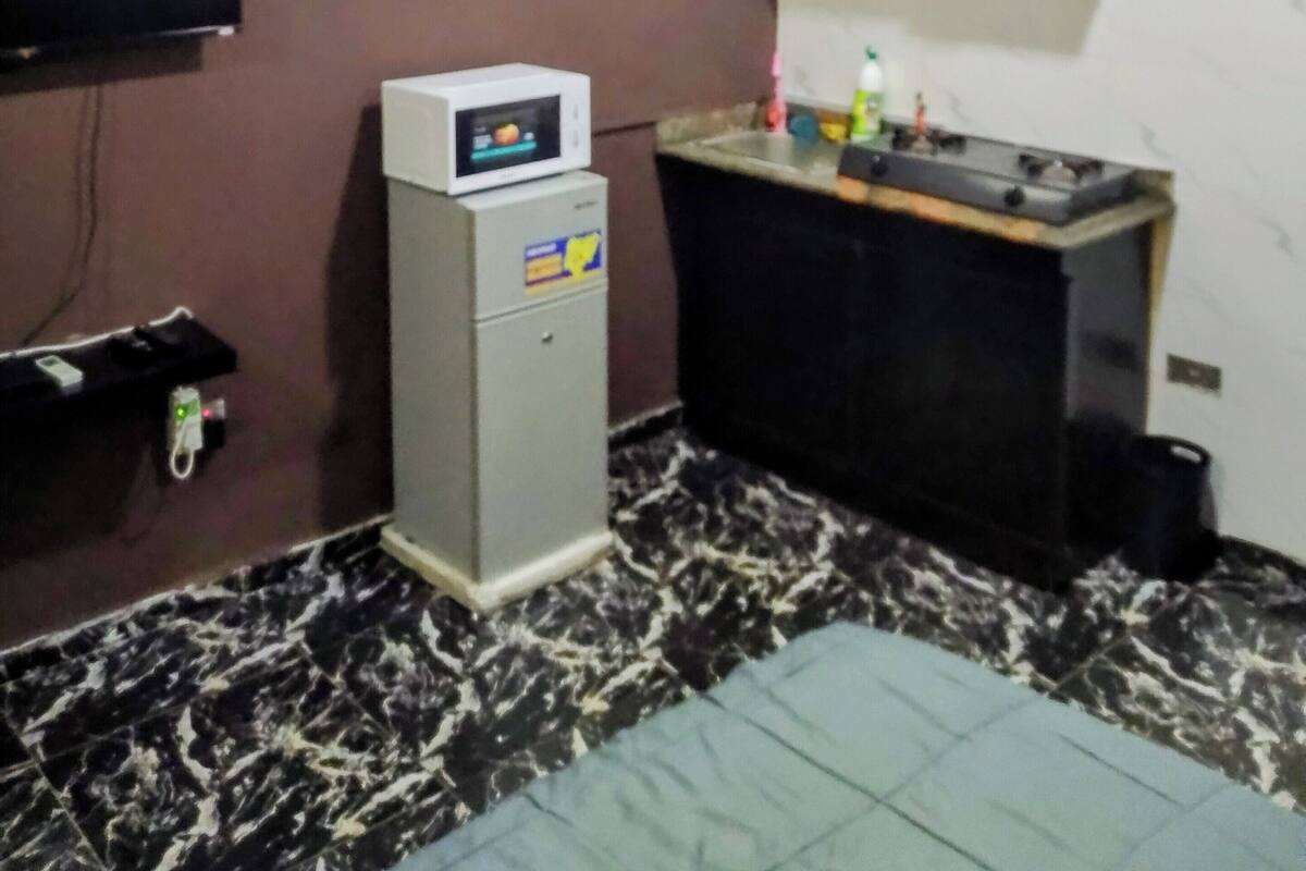 Une cuisine compacte équipée d’un four à micro-ondes, d’un petit réfrigérateur, d’un évier et d’une armoire en bois située au-dessus.