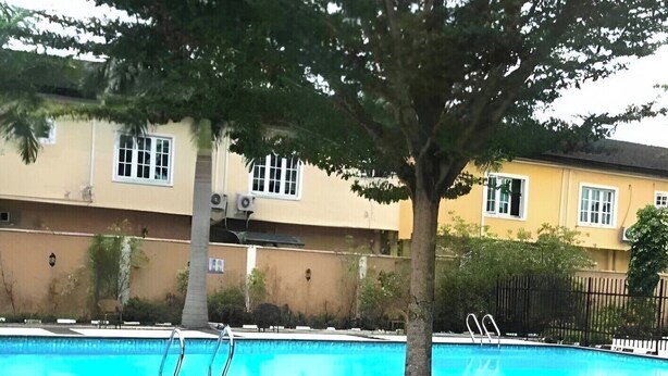 A swimming pool with a tree in the foreground, surrounded by a grassy area. - Short Let in lagos business school Ajah  (Lekki)