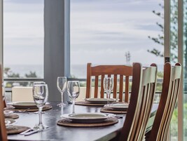 Una mesa de comedor dispuesta con platos, cubiertos y copas de vino, con sillas de madera y vistas al exterior.
