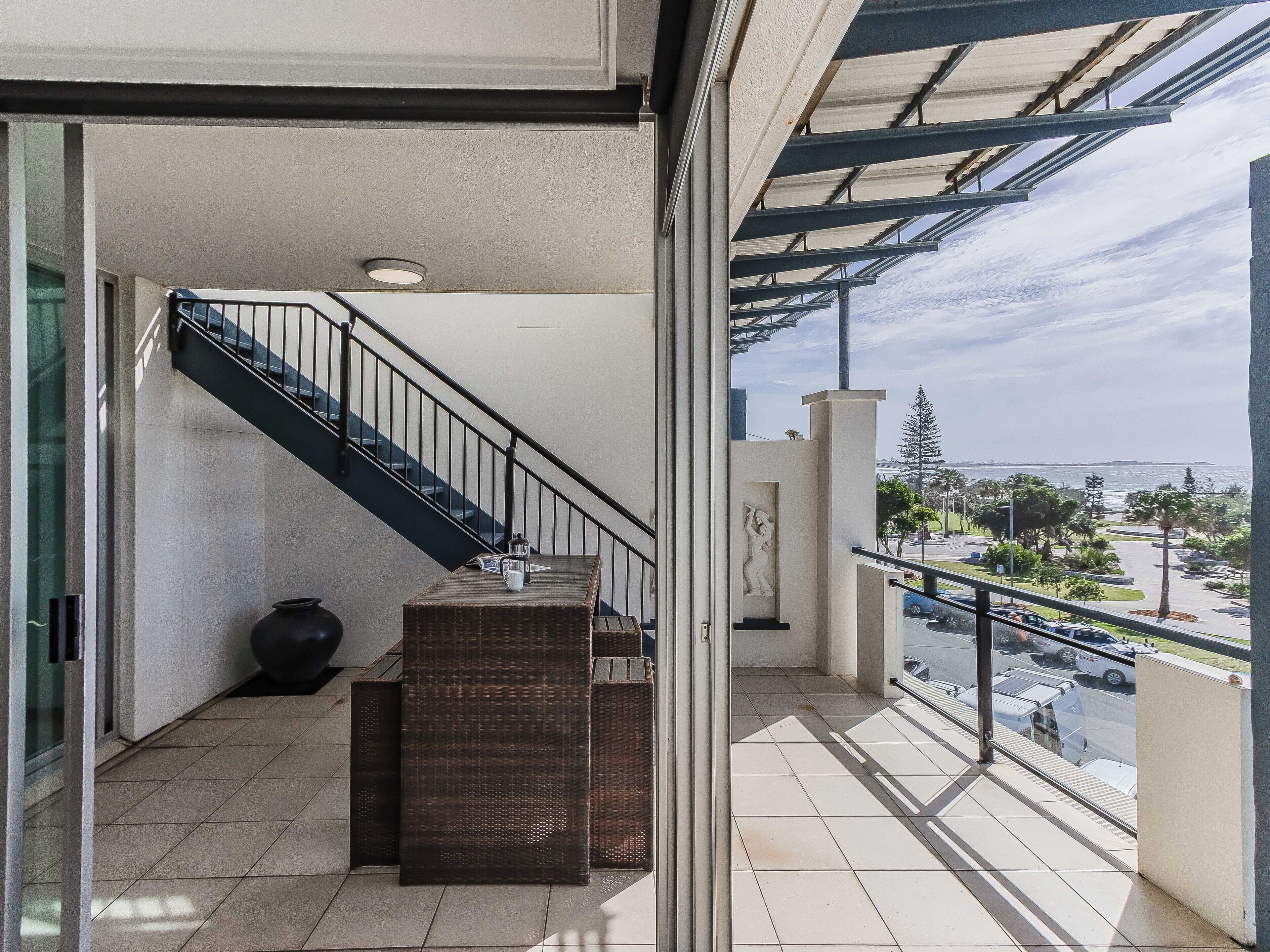 A balcony with a view of a parking area and a distant body of water.