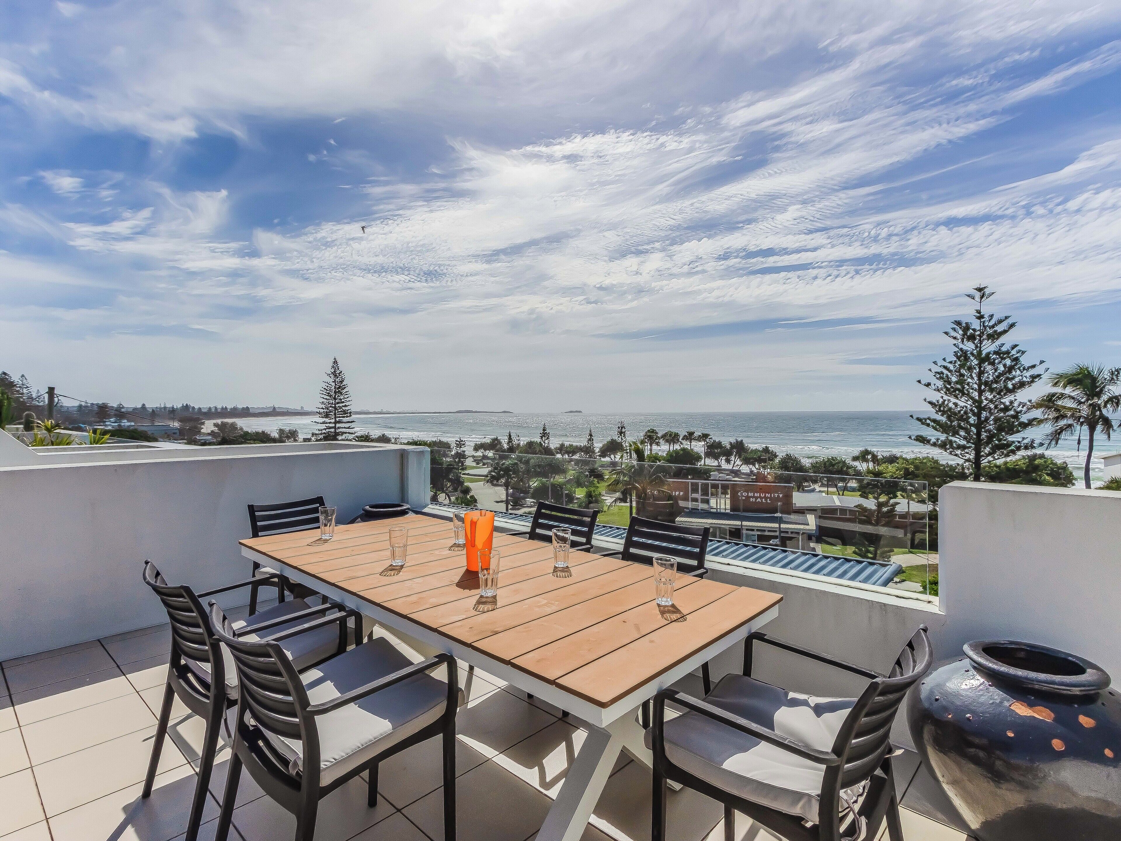 A terrace with a table and chairs, overlooking a coastal view with a building labeled 'Community Hall' in the background.