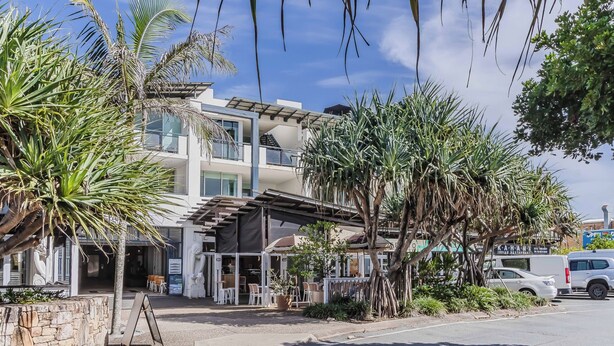 A multi-story building with a covered outdoor seating area, palm trees, and a parked car. - Paradiso Paradise 336 3BRM Oceanfront (Kingscliff)
