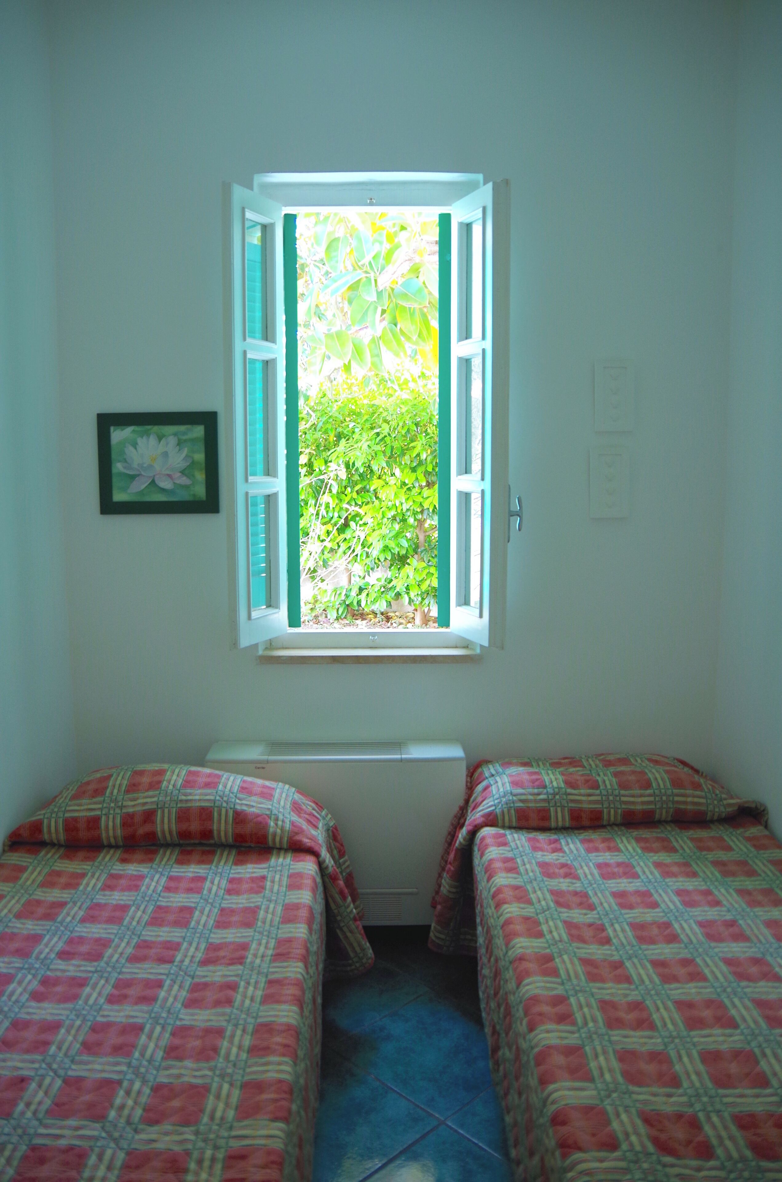 Una habitación con dos camas, una ventana con contraventanas abiertas y un cuadro en la pared.