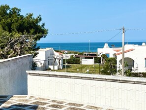 Ein Küstenwohngebiet mit weißen Häusern, freiem Blick auf das Meer und einem gepflasterten Gehweg.